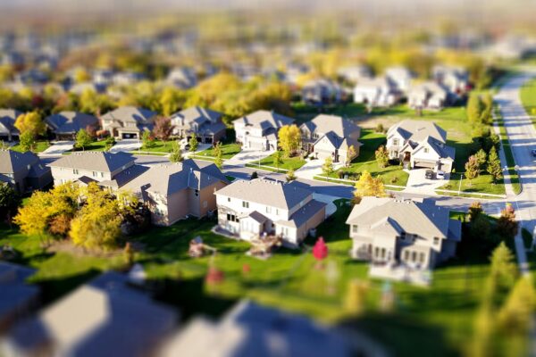 Tilt-shift aerial photo of a suburban neighborhood with green lawns and roads.